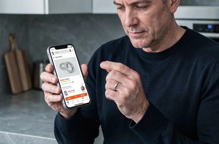 Homme comparant un bijou reçu avec les informations d'un site de vente en ligne sur son smartphone pour éviter les arnaques
